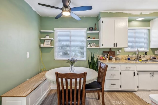 kitchen featuring ceiling fan, sink, white cabinetry, and light hardwood / wood-style flooring