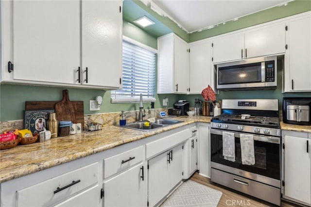 kitchen with light wood-type flooring, stainless steel appliances, white cabinets, and sink