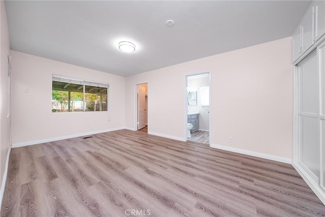 unfurnished bedroom with ensuite bathroom, a closet, and light wood-type flooring