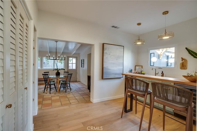 kitchen featuring an inviting chandelier, light hardwood / wood-style floors, hanging light fixtures, and beamed ceiling