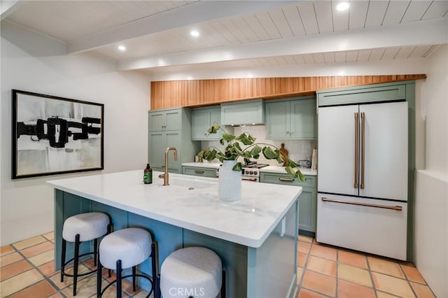 kitchen with sink, lofted ceiling with beams, a breakfast bar, a center island with sink, and high end fridge