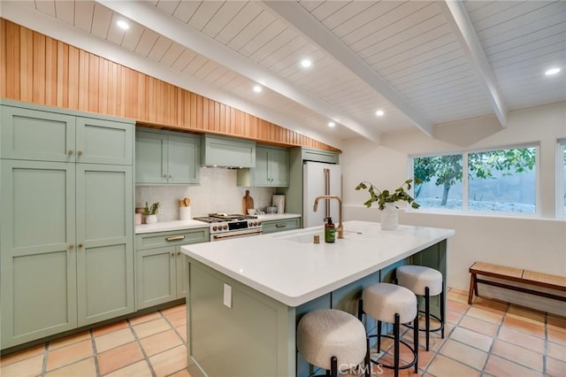 kitchen featuring backsplash, a center island with sink, green cabinets, high end appliances, and a kitchen breakfast bar