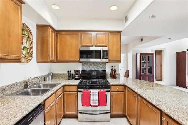 kitchen featuring kitchen peninsula, appliances with stainless steel finishes, tasteful backsplash, light stone counters, and sink