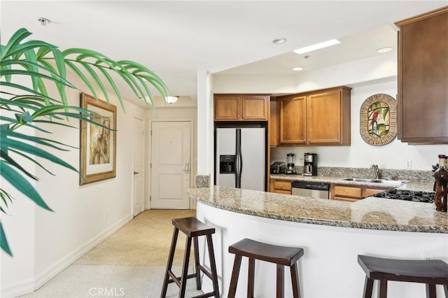 kitchen with a kitchen bar, white fridge with ice dispenser, stainless steel dishwasher, light stone counters, and sink