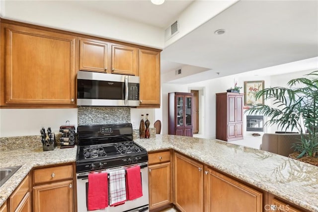 kitchen featuring gas range oven, backsplash, kitchen peninsula, and light stone countertops