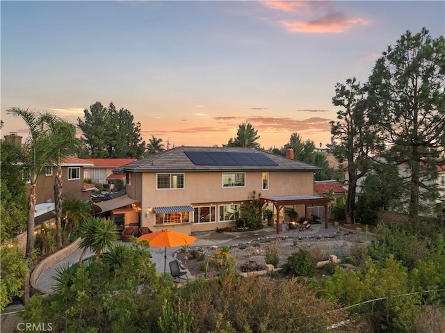 back house at dusk featuring a patio area and solar panels