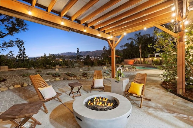 patio terrace at dusk featuring an outdoor fire pit, a mountain view, and a fenced in pool