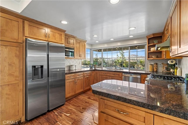 kitchen featuring kitchen peninsula, stainless steel appliances, backsplash, dark hardwood / wood-style flooring, and wall chimney exhaust hood