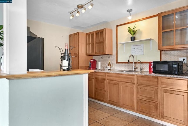 kitchen with tasteful backsplash, black appliances, sink, light tile patterned floors, and light stone counters