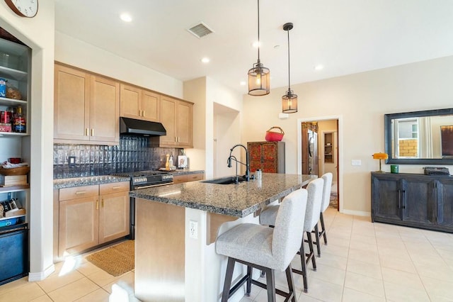 kitchen featuring decorative light fixtures, stainless steel range, dark stone counters, sink, and a kitchen island with sink