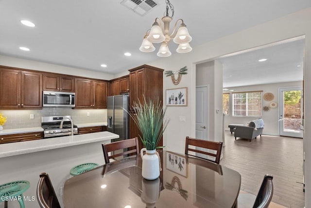 kitchen featuring appliances with stainless steel finishes, backsplash, hanging light fixtures, a chandelier, and light hardwood / wood-style flooring