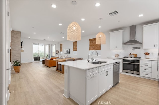 kitchen with appliances with stainless steel finishes, wall chimney exhaust hood, white cabinets, and sink