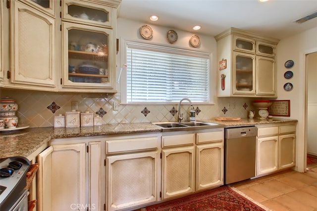 kitchen featuring tasteful backsplash, stainless steel dishwasher, sink, light tile patterned floors, and cream cabinetry