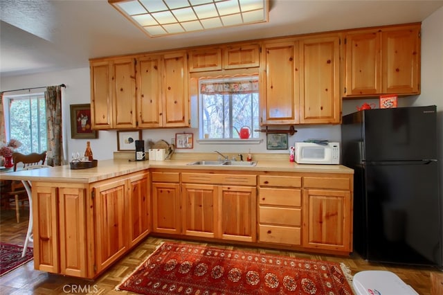 kitchen with black fridge, light parquet floors, kitchen peninsula, and sink