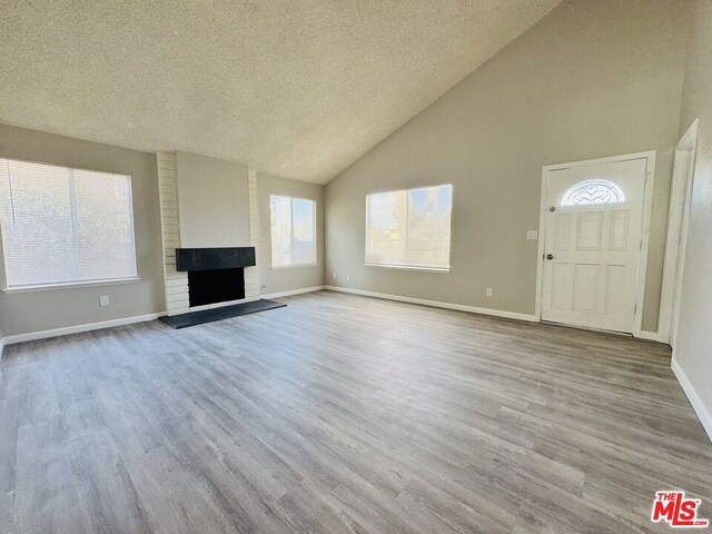 unfurnished living room featuring a textured ceiling, a fireplace, light hardwood / wood-style flooring, and high vaulted ceiling