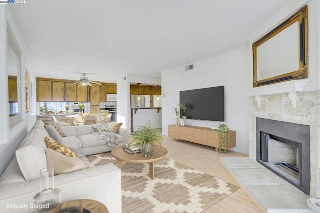 living room with ceiling fan, light hardwood / wood-style floors, and a tiled fireplace