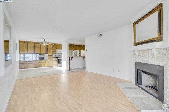 unfurnished living room featuring ceiling fan, a tiled fireplace, and light hardwood / wood-style flooring