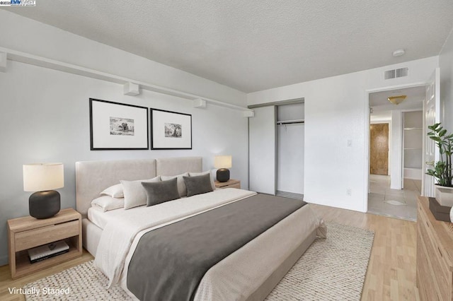 bedroom featuring light wood-type flooring, a closet, a textured ceiling, and connected bathroom