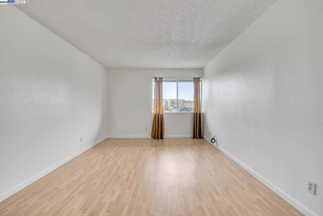 spare room with light wood-type flooring and a textured ceiling