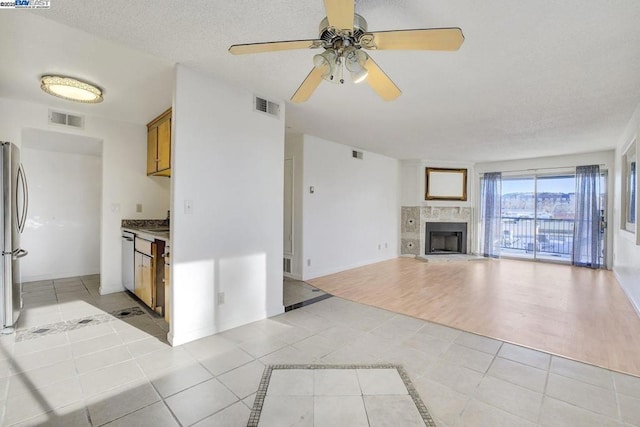 kitchen with light tile patterned floors, ceiling fan, stainless steel appliances, a fireplace, and a textured ceiling