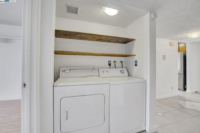 laundry room featuring a textured ceiling, light tile patterned floors, and washing machine and clothes dryer