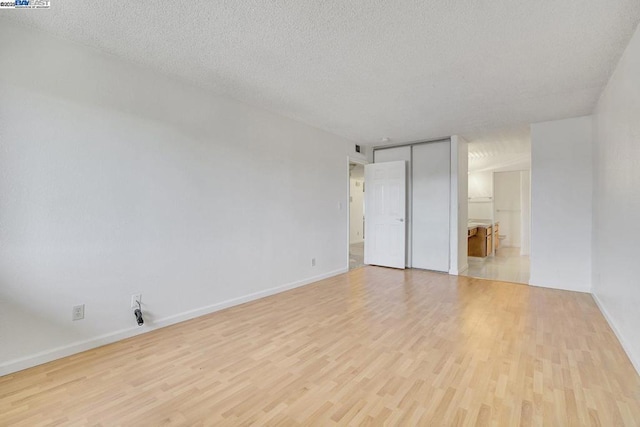 unfurnished bedroom featuring a textured ceiling, a closet, connected bathroom, and light wood-type flooring