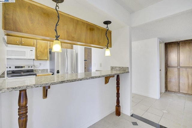 kitchen with a kitchen breakfast bar, appliances with stainless steel finishes, light tile patterned flooring, and hanging light fixtures