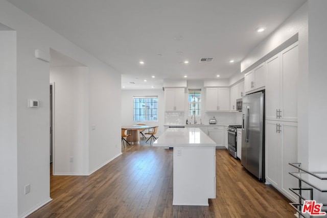 kitchen featuring appliances with stainless steel finishes, decorative backsplash, a center island, white cabinets, and sink