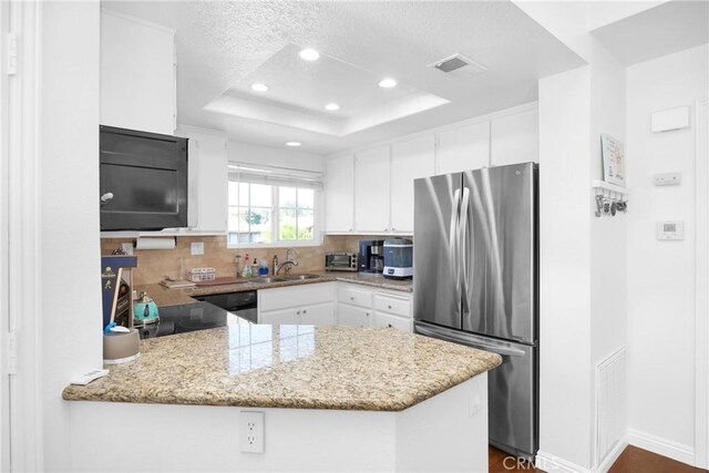 kitchen with kitchen peninsula, white cabinetry, a tray ceiling, and stainless steel refrigerator