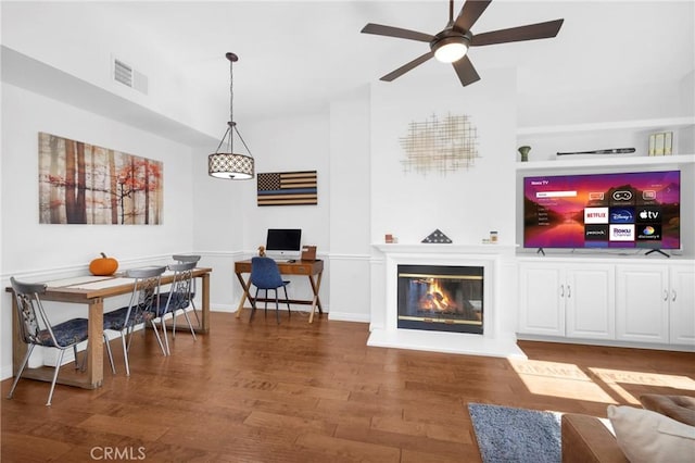 living room with wood finished floors, baseboards, visible vents, a ceiling fan, and a glass covered fireplace