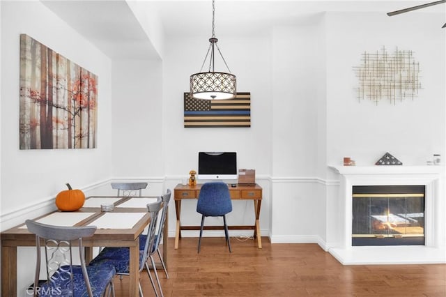 office featuring a glass covered fireplace, baseboards, and wood finished floors