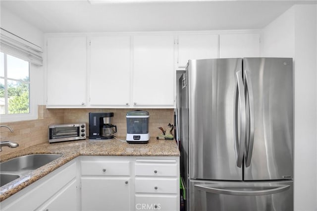 kitchen featuring decorative backsplash, white cabinetry, freestanding refrigerator, and a sink