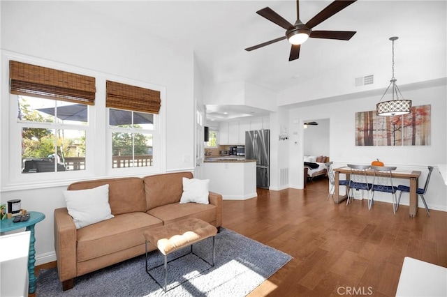 living room featuring visible vents, dark wood-type flooring, a ceiling fan, baseboards, and vaulted ceiling