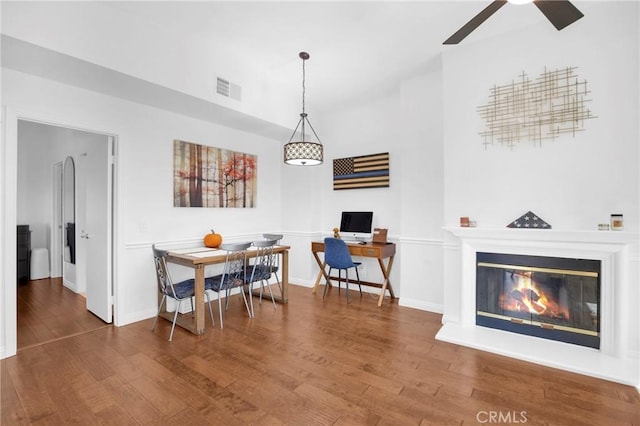 dining room with a glass covered fireplace, visible vents, baseboards, and wood finished floors