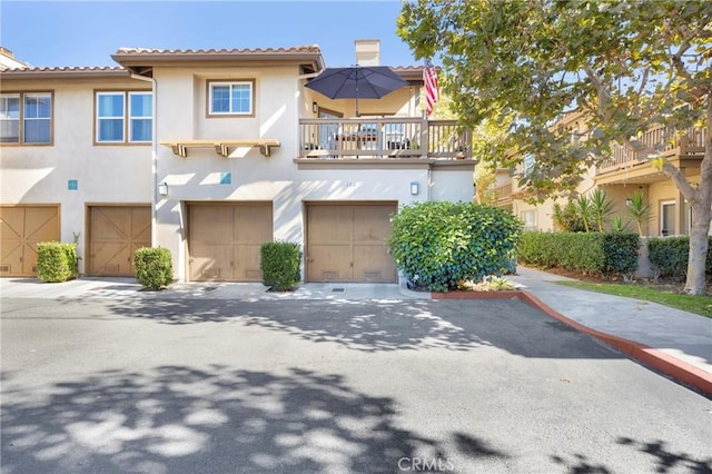 townhome / multi-family property with driveway, an attached garage, a chimney, stucco siding, and a tile roof