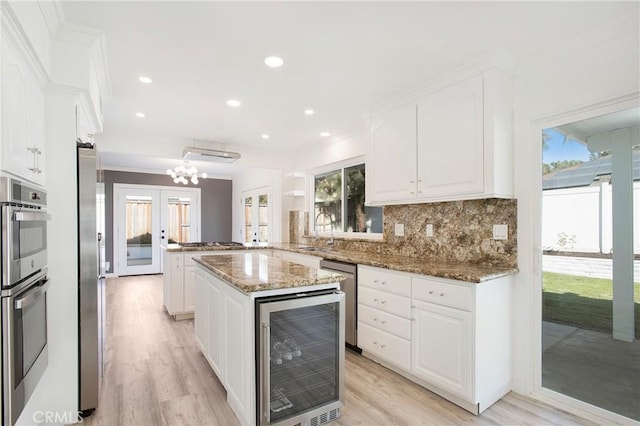 kitchen with wine cooler, french doors, white cabinetry, stone countertops, and a center island