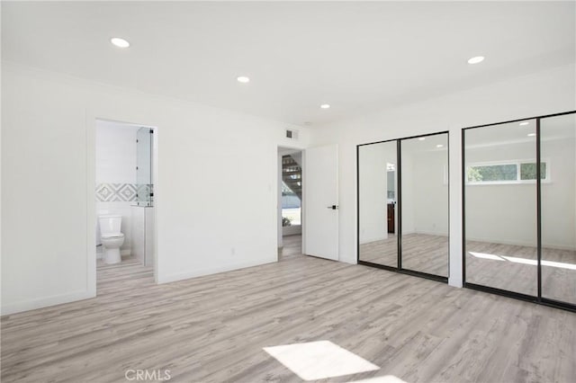 unfurnished bedroom featuring connected bathroom, two closets, and light wood-type flooring