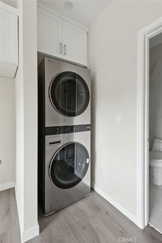 washroom with cabinets, stacked washer and clothes dryer, and light hardwood / wood-style floors