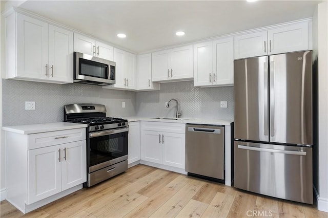 kitchen featuring stainless steel appliances, tasteful backsplash, light wood-type flooring, white cabinets, and sink