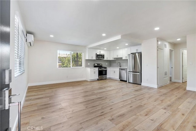 kitchen featuring white cabinets, appliances with stainless steel finishes, decorative backsplash, light wood-type flooring, and a wall mounted air conditioner