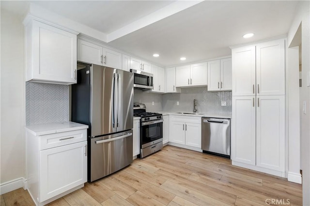 kitchen featuring stainless steel appliances, backsplash, light wood-type flooring, white cabinets, and sink