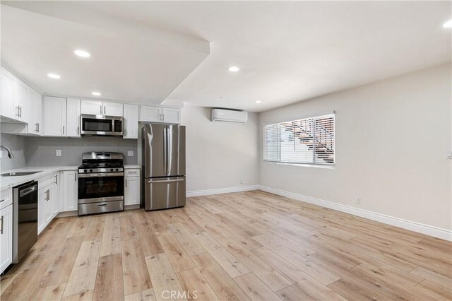 kitchen featuring an AC wall unit, sink, light wood-type flooring, appliances with stainless steel finishes, and white cabinets