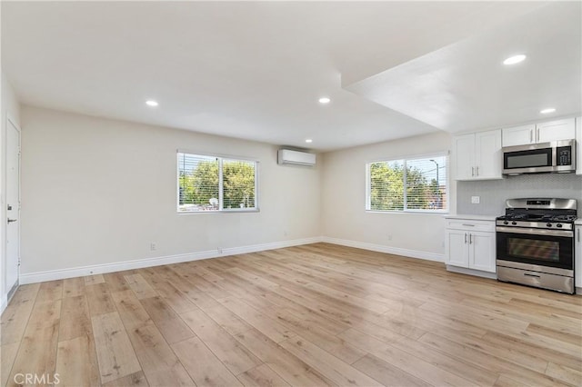 kitchen with backsplash, white cabinetry, appliances with stainless steel finishes, and a wall unit AC