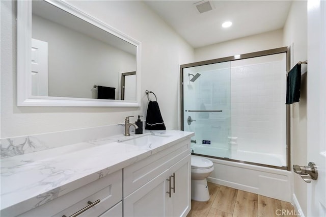 full bathroom with toilet, hardwood / wood-style flooring, vanity, and shower / bath combination with glass door