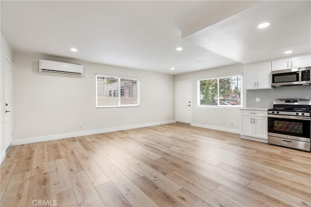 kitchen featuring white cabinetry, a wall unit AC, appliances with stainless steel finishes, decorative backsplash, and light wood-type flooring