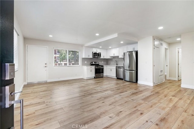 kitchen with appliances with stainless steel finishes, light hardwood / wood-style floors, white cabinetry, and sink