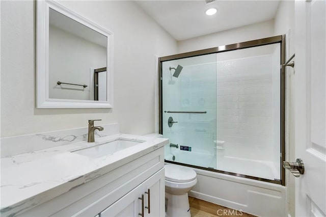 full bathroom featuring wood-type flooring, combined bath / shower with glass door, vanity, and toilet