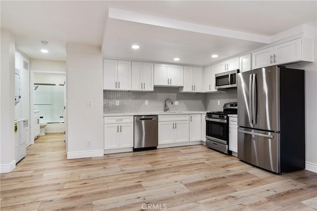 kitchen with appliances with stainless steel finishes, white cabinetry, tasteful backsplash, light hardwood / wood-style floors, and sink