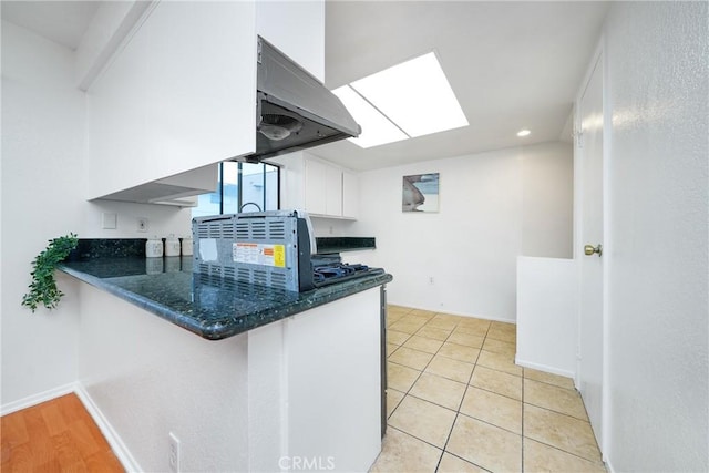 kitchen featuring light tile patterned floors, white cabinetry, extractor fan, and kitchen peninsula