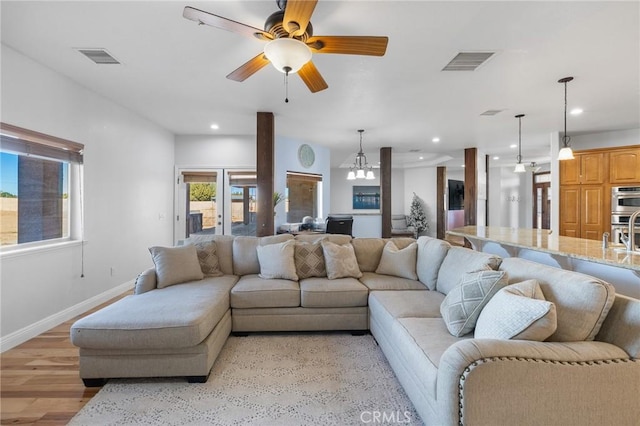 living room with ceiling fan with notable chandelier and light hardwood / wood-style flooring